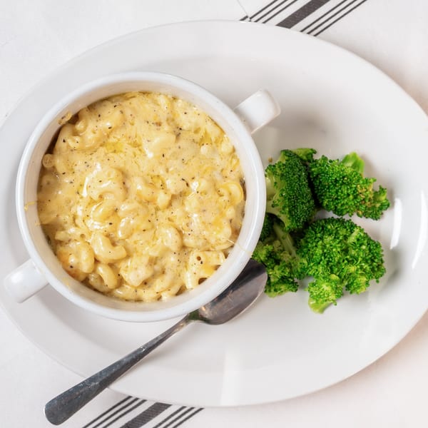 Creamy mac and cheese in a white bowl with a side of bright green broccoli florets and a spoon.