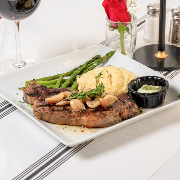 Grilled steak with roasted garlic, mashed potatoes, asparagus, and a side of green sauce.