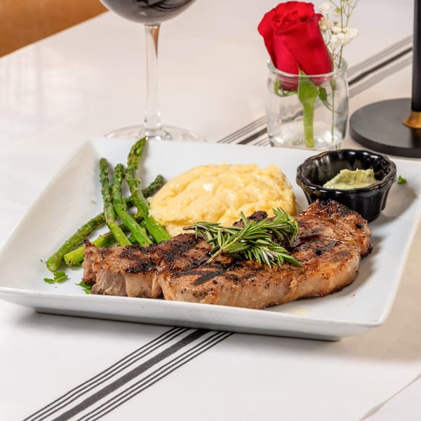 Grilled steak with rosemary, mashed potatoes, asparagus, and a red wine glass on a white plate.