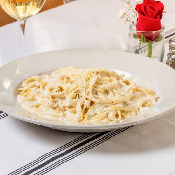 Creamy fettuccine alfredo with grated cheese, a glass of white wine, and a red rose.