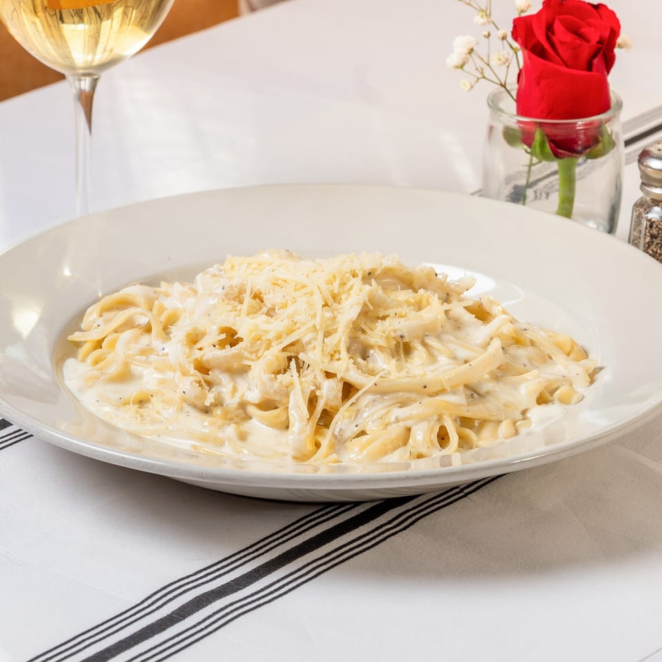 Creamy fettuccine alfredo with grated cheese, a glass of white wine, and a red rose.