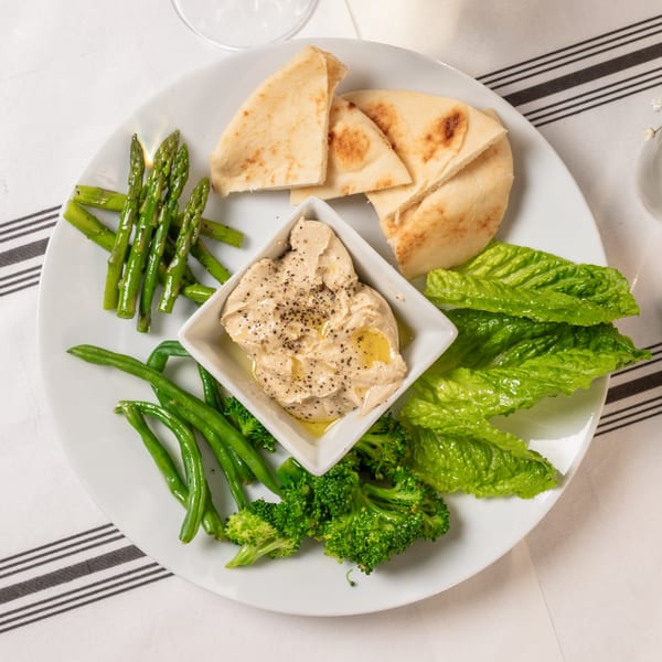 A white plate with hummus, pita bread, asparagus, green beans, broccoli, and lettuce.