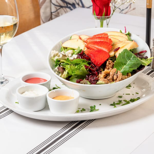 A fresh salad with strawberries, apples, walnuts, and cheese, served with three dressings.