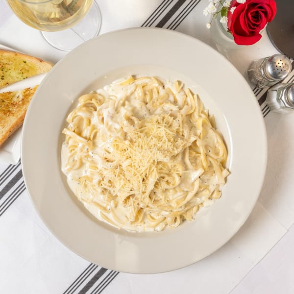 Creamy fettuccine alfredo topped with grated cheese, served with garlic bread and white wine.