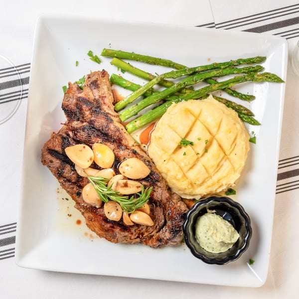 Grilled steak with roasted garlic, rosemary, mashed potatoes, asparagus, and a side of green sauce.