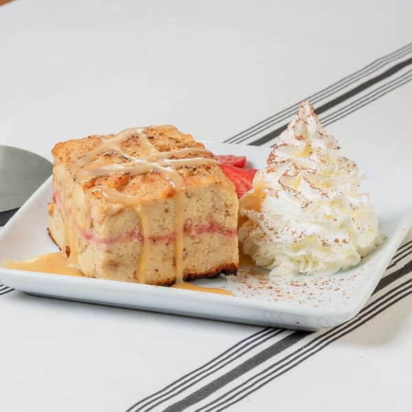 Bread pudding with caramel drizzle, whipped cream, and sliced strawberries on a white plate.