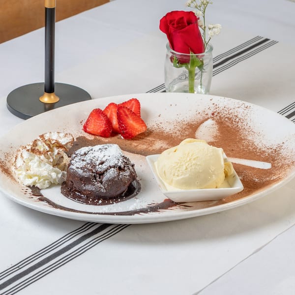 Chocolate lava cake with whipped cream, strawberries, and vanilla ice cream on a white plate.