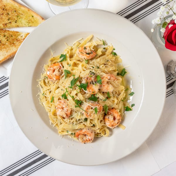 Shrimp fettuccine alfredo with parsley and parmesan, garlic bread, and a rose on a striped napkin.