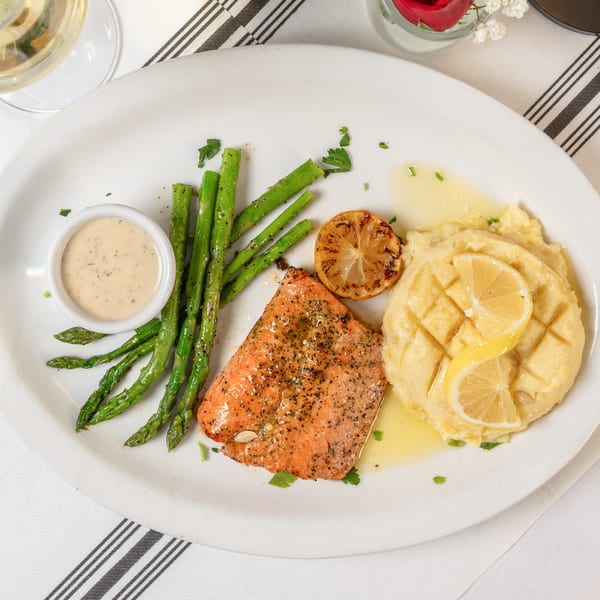 Grilled salmon with asparagus, mashed potatoes, a lemon slice, and dipping sauce on a white plate.
