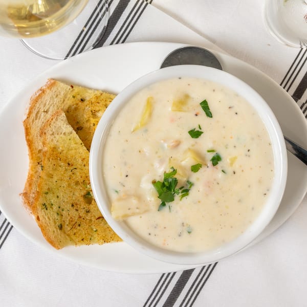 Creamy clam chowder with parsley in a white bowl, served with two slices of garlic bread.