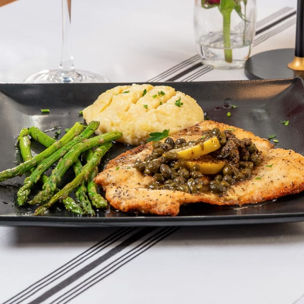 Pan-seared fish with capers and lemon, mashed potatoes, and asparagus on a black plate.