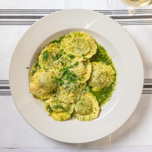 Ravioli with green pesto sauce, grated cheese, and fresh parsley on a white plate.